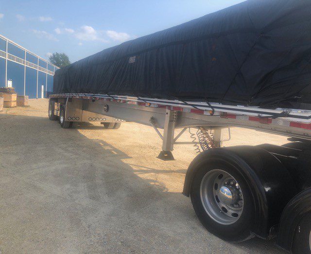 Large flatbed trailer carrying expedited freight under a heavy tarp.